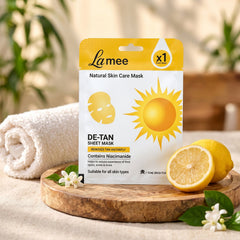 White and yellow sheet mask package with sun and face icons, lemons, and a white towel on a wooden tray.