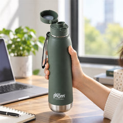 A person's hand holds an open dark green insulated stainless steel water bottle with a flip lid at a desk with a laptop and