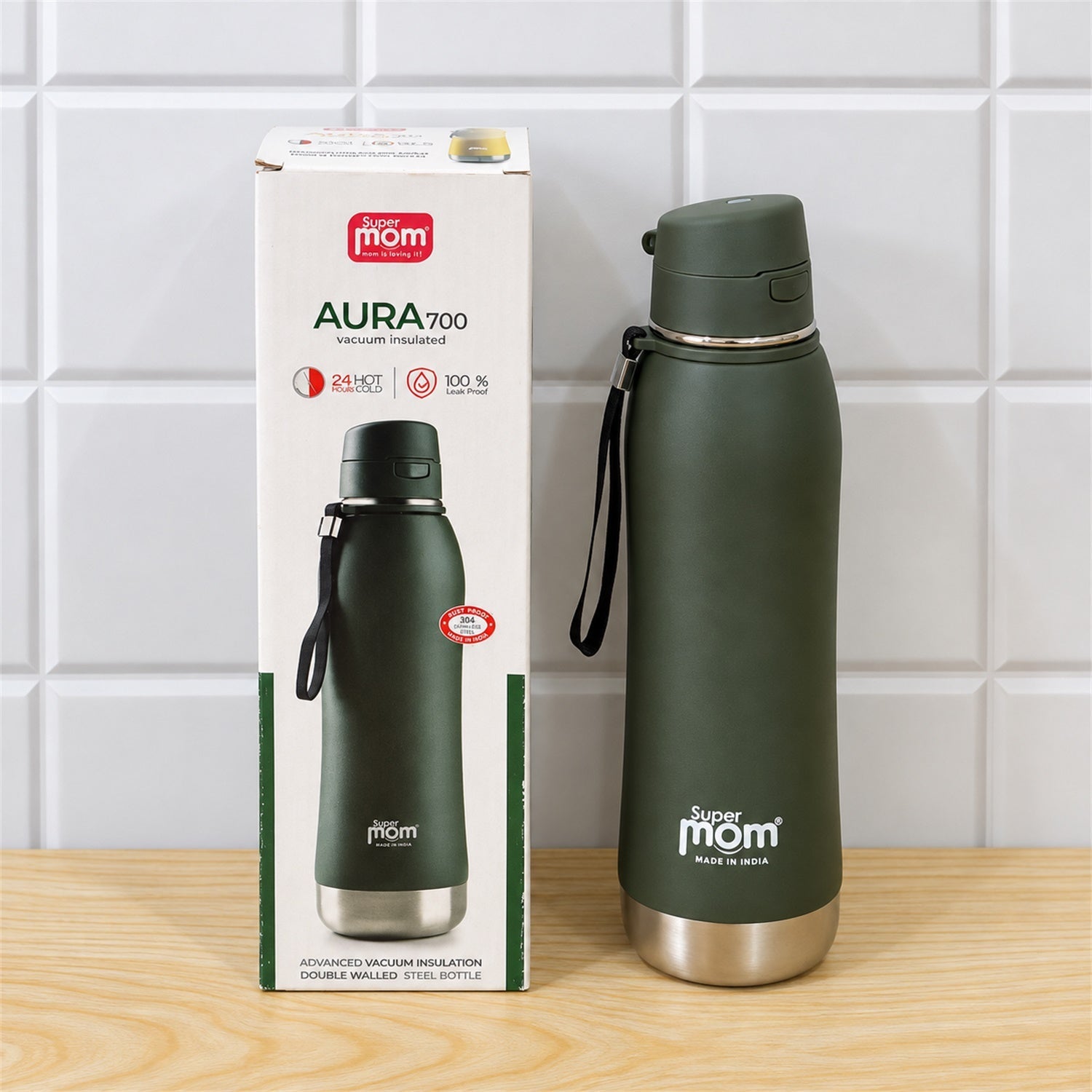 A dark green insulated stainless steel water bottle stands next to its product packaging on a wooden surface against white