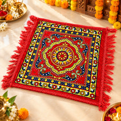 A red square prayer mat with a colorful traditional design and red fringe, placed on a light-colored floor.