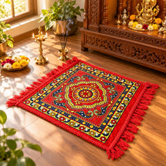 A red prayer mat with a vibrant traditional pattern and fringe, positioned on a wooden floor near a decorative altar.