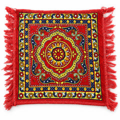 A square red prayer mat with a detailed yellow and blue traditional pattern and red fringe, viewed from above.