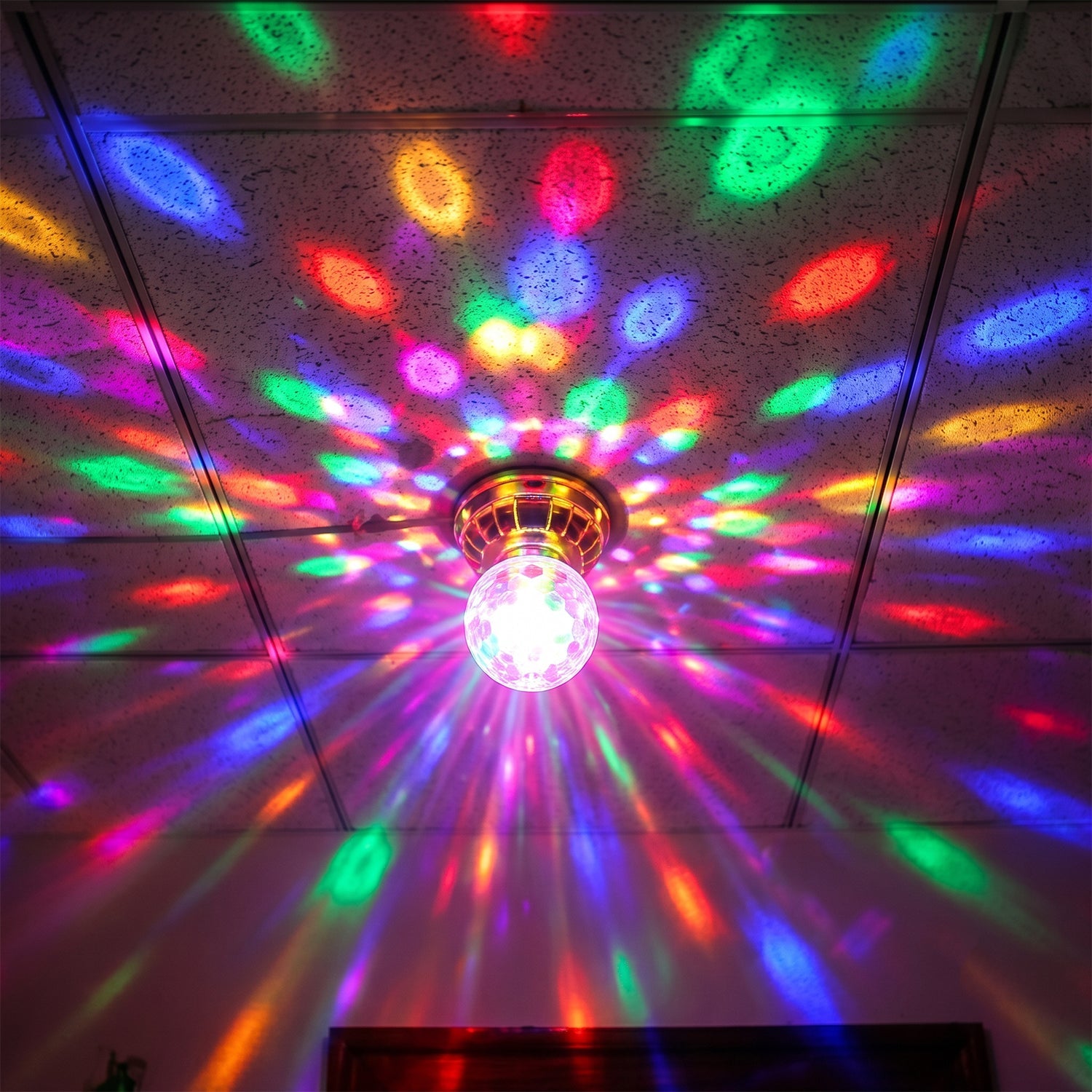 A gold and clear disco bulb is screwed into a ceiling, projecting a vibrant, colorful light pattern across the entire room.