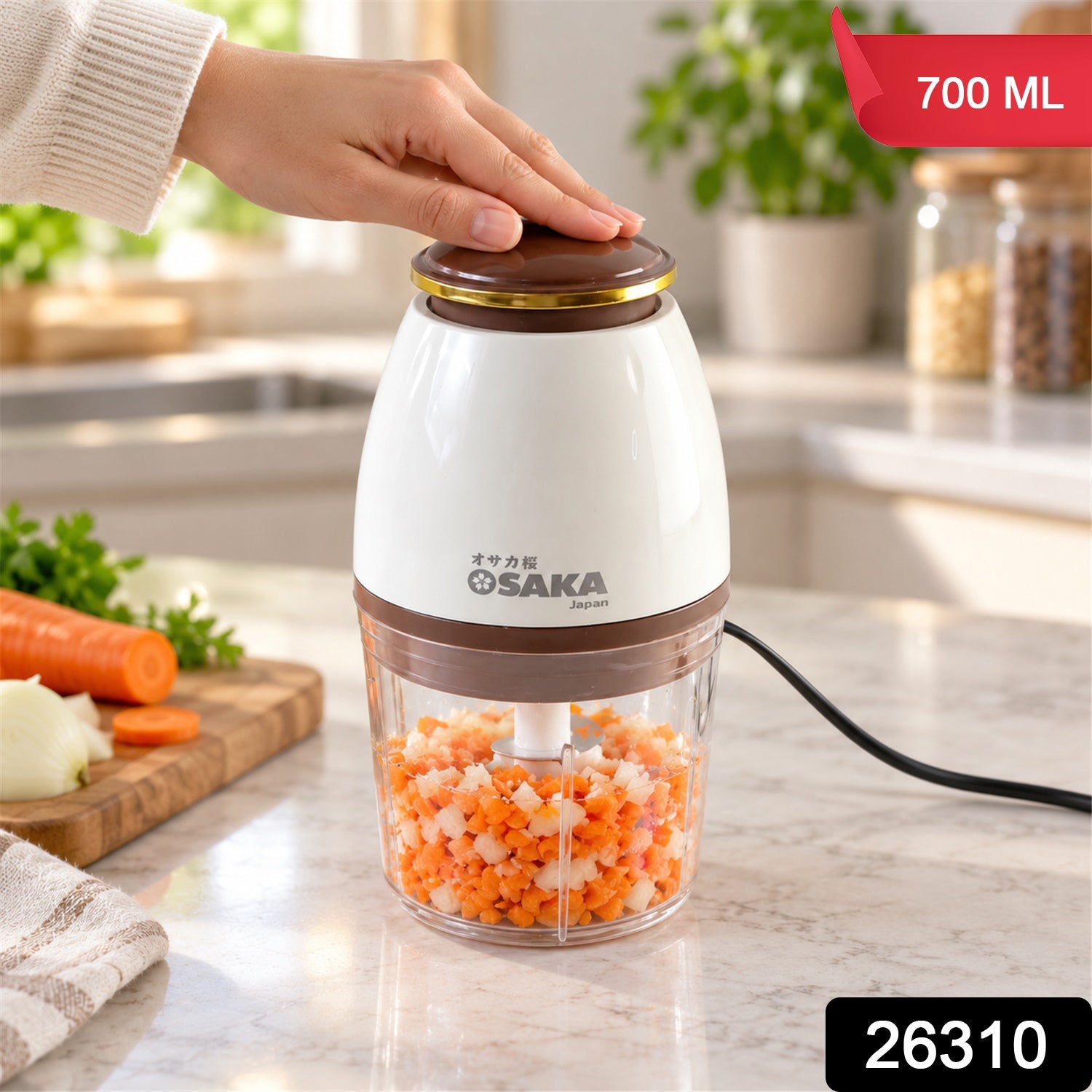 A hand operates a white and clear electric chopper on a kitchen counter, filled with finely chopped vegetables.