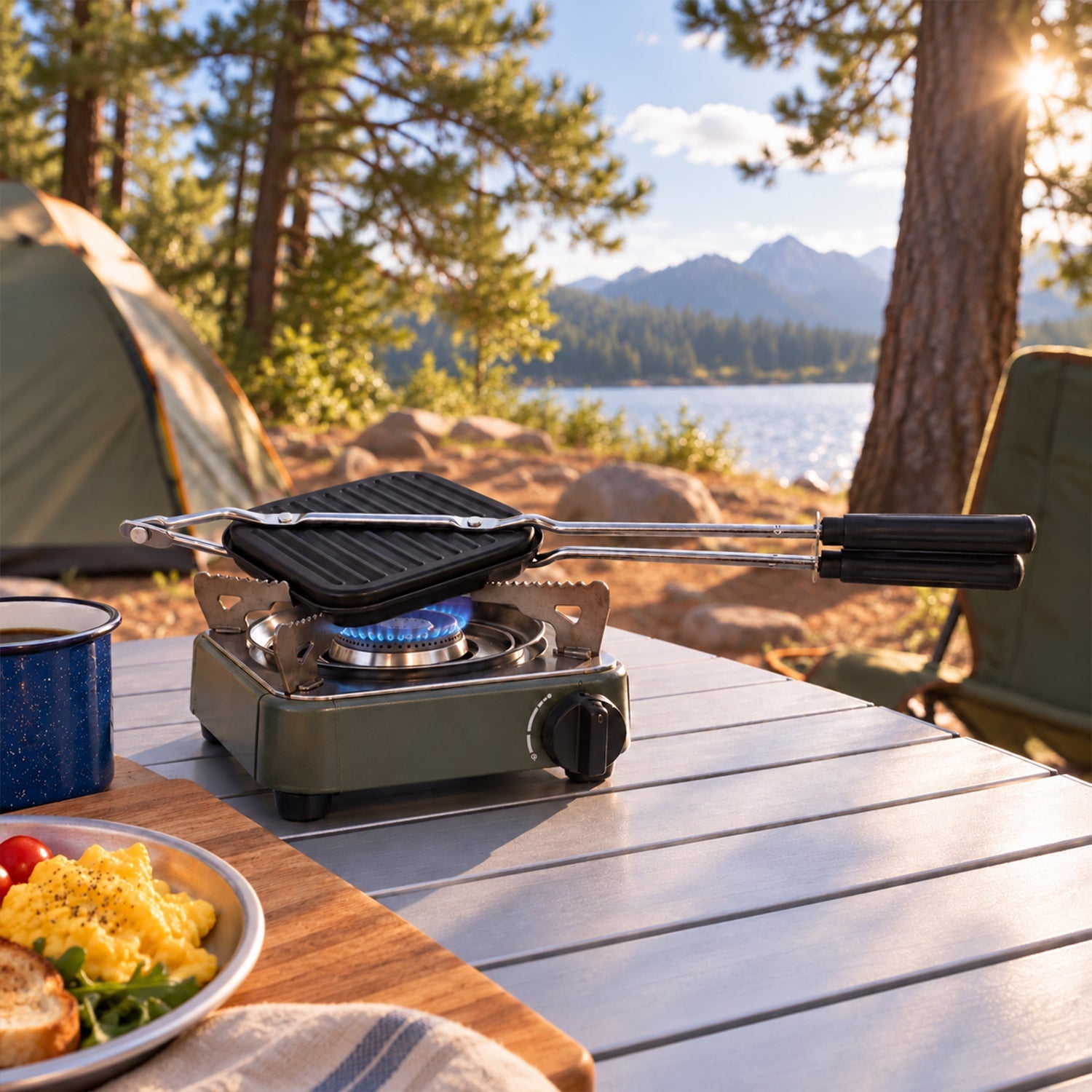 Black sandwich maker cooking on a portable gas stove at a campsite by a lake, with a tent and trees visible.