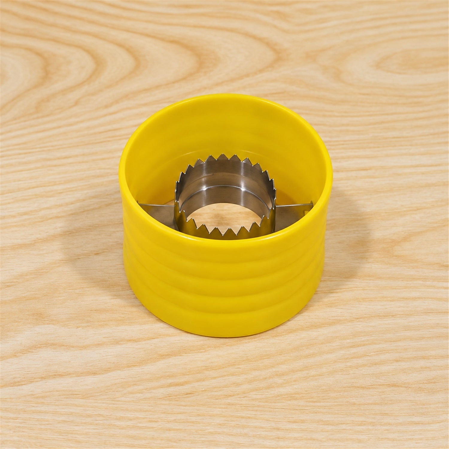 A yellow corn stripper with a silver serrated interior sits centered on a light wooden table.