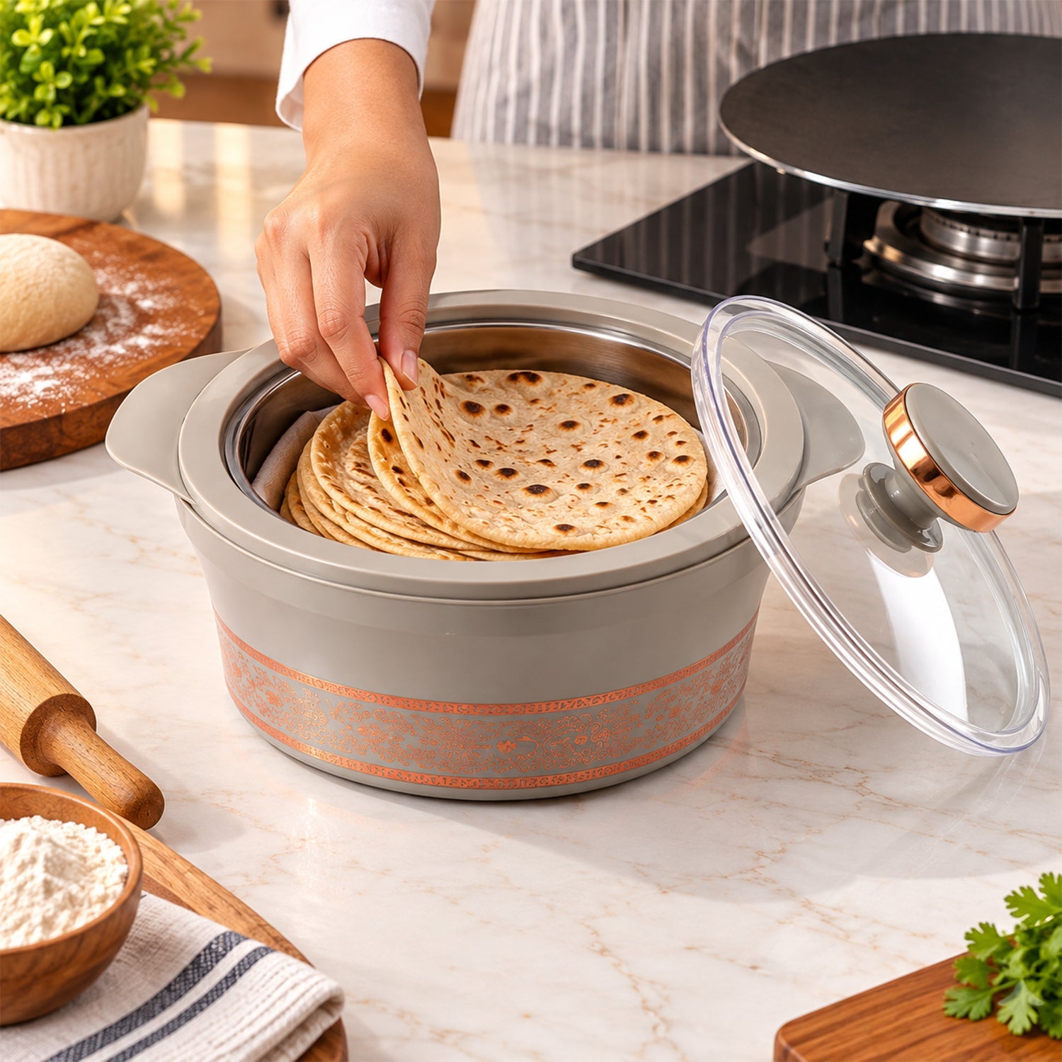 A person places flatbread into a gray insulated casserole dish with a stainless steel interior on a kitchen counter.
