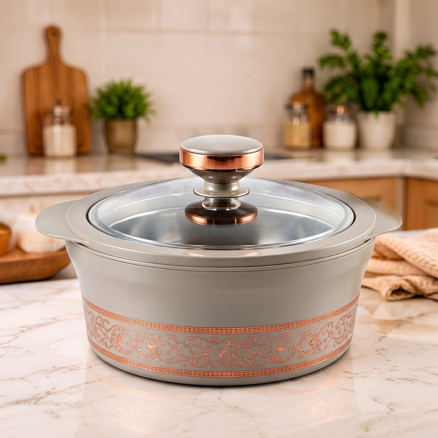 A gray insulated casserole dish with a clear lid and copper accents sits on a bright kitchen counter.