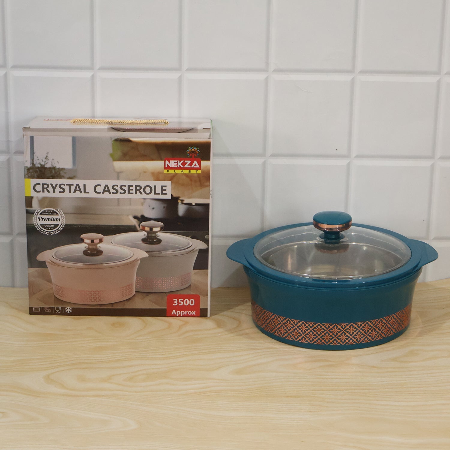 A teal insulated casserole dish with a clear lid, next to its product box, on a wooden surface.