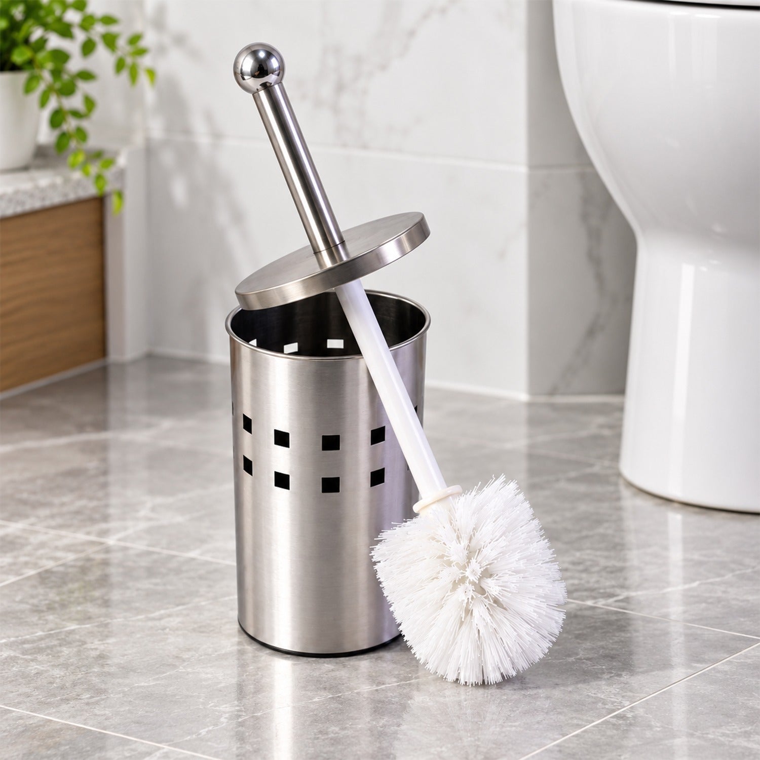 A stainless steel toilet brush holder with a white brush partially extended, sitting on a tiled bathroom floor next to a