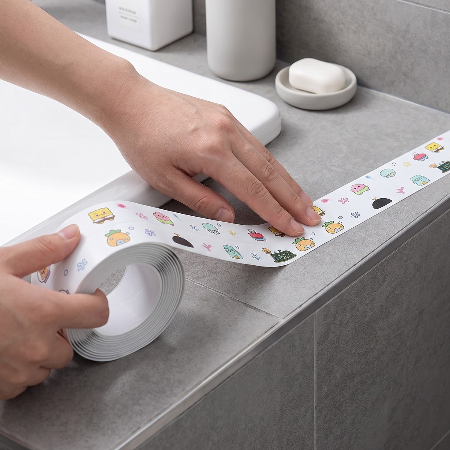 Hands applying white cartoon-printed sealing tape around a bathroom sink edge, with a small inset showing the tape â€“ view 7