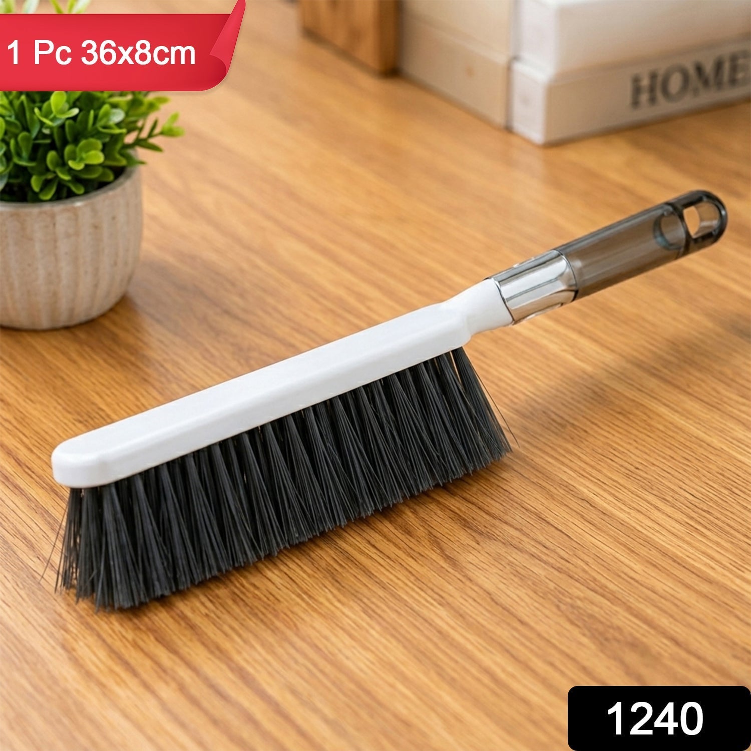 A white and gray cleaning brush with dark bristles rests on a light wooden surface next to a small potted plant. â€“ view 9
