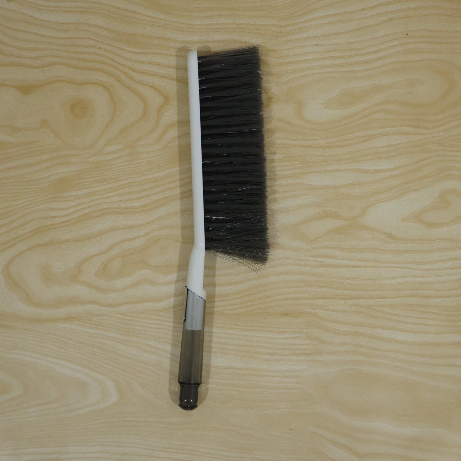 The white and gray cleaning brush is positioned vertically on a light wood grain background.