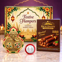 A gold Ganesh kumkum dish, a box of hazelnut wafer rolls, and a silver coin, with a festive hamper box in the background and