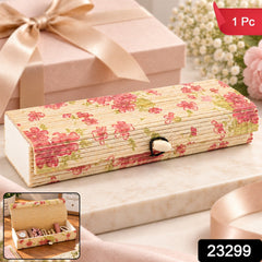 A decorative bamboo box with a floral design and roll-top lid on a marble surface, with a pink gift box in the background.