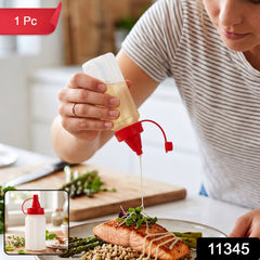 A person drizzles oil from a clear plastic squeeze bottle with a red cap onto salmon and asparagus. â€“ view 2
