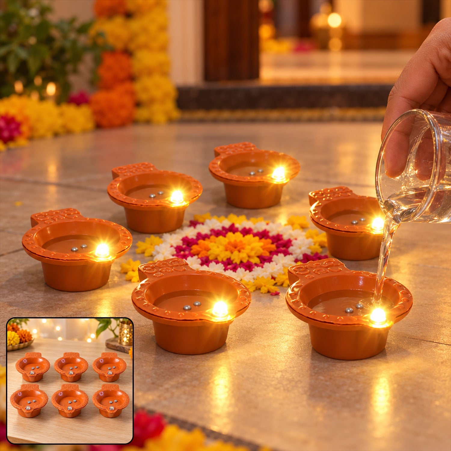 A hand pours water into one of six glowing orange diyas, arranged on a floor with a colorful floral design.
