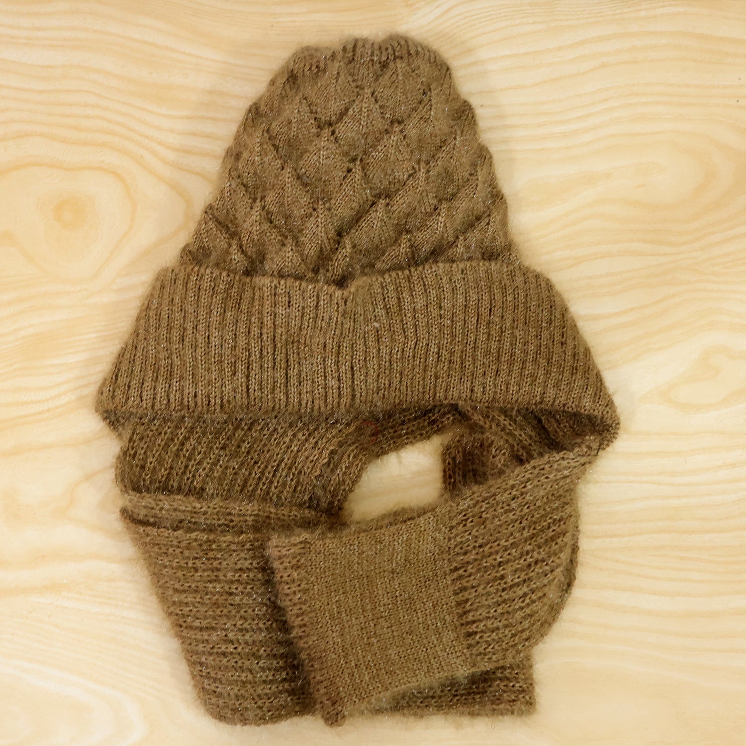 A brown knitted cap with an attached scarf is laid flat on a light wood surface, showcasing its texture.