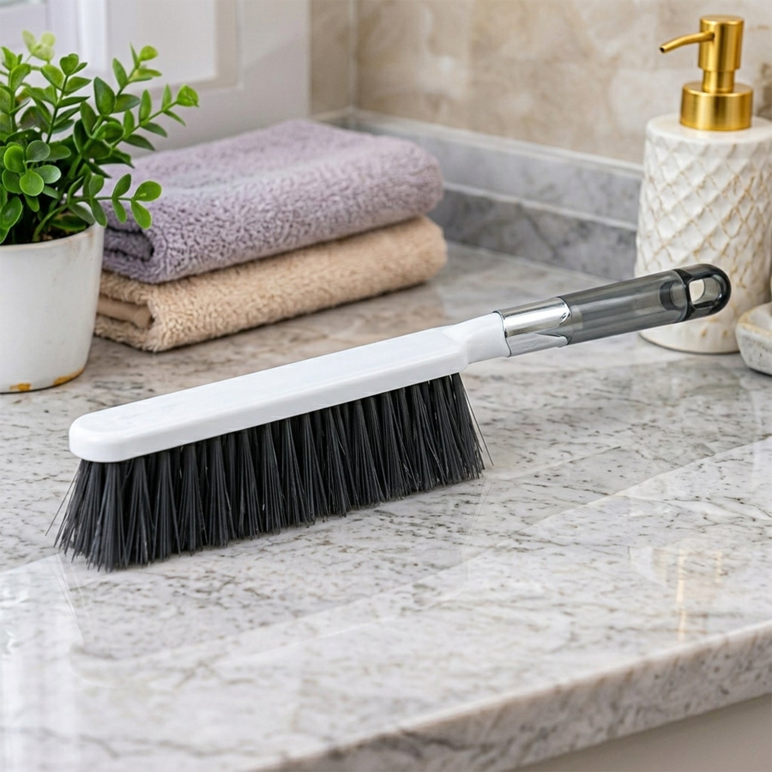 The white and gray cleaning brush sits on a speckled marble countertop near folded towels and a soap dispenser.