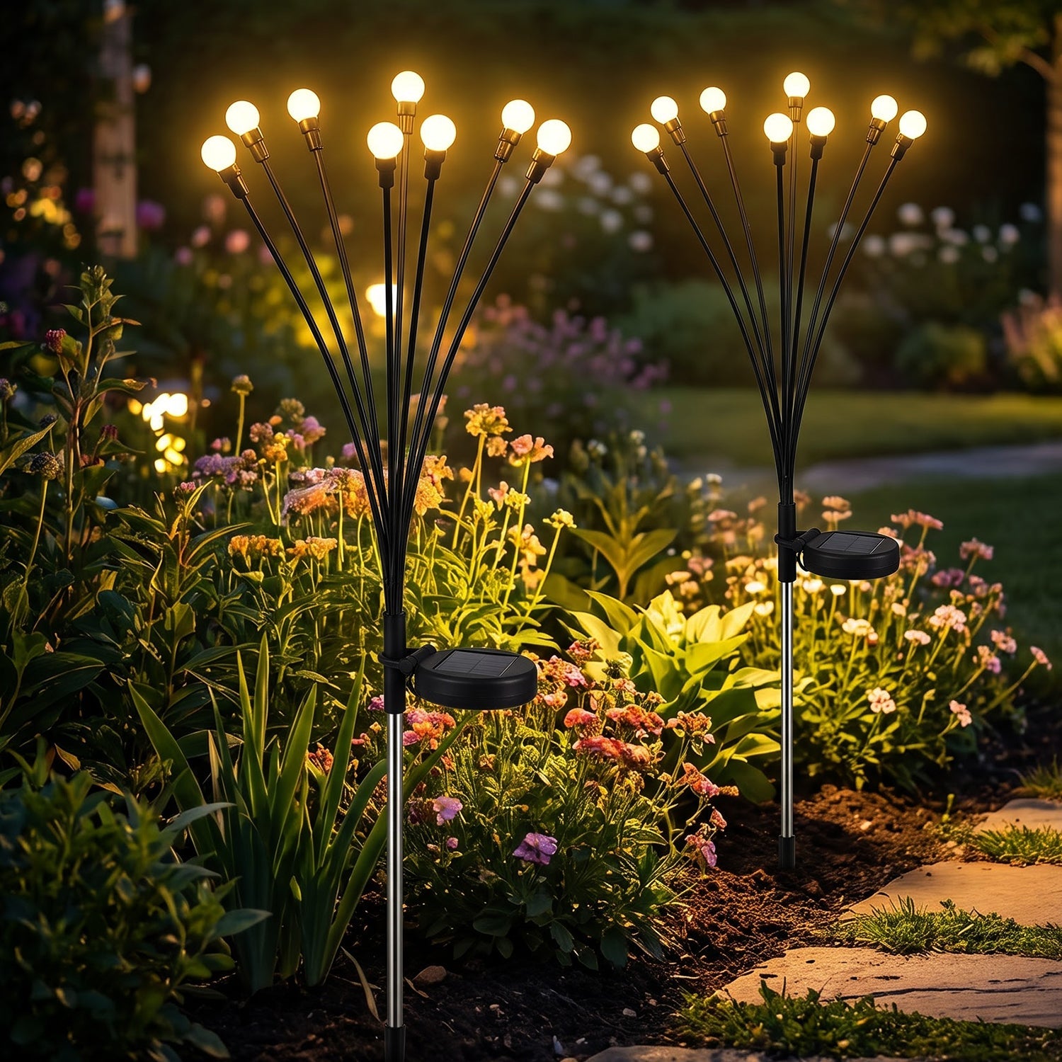 Two solar firefly lights with bright bulbs glow amidst green foliage and colorful flowers in a garden at night.