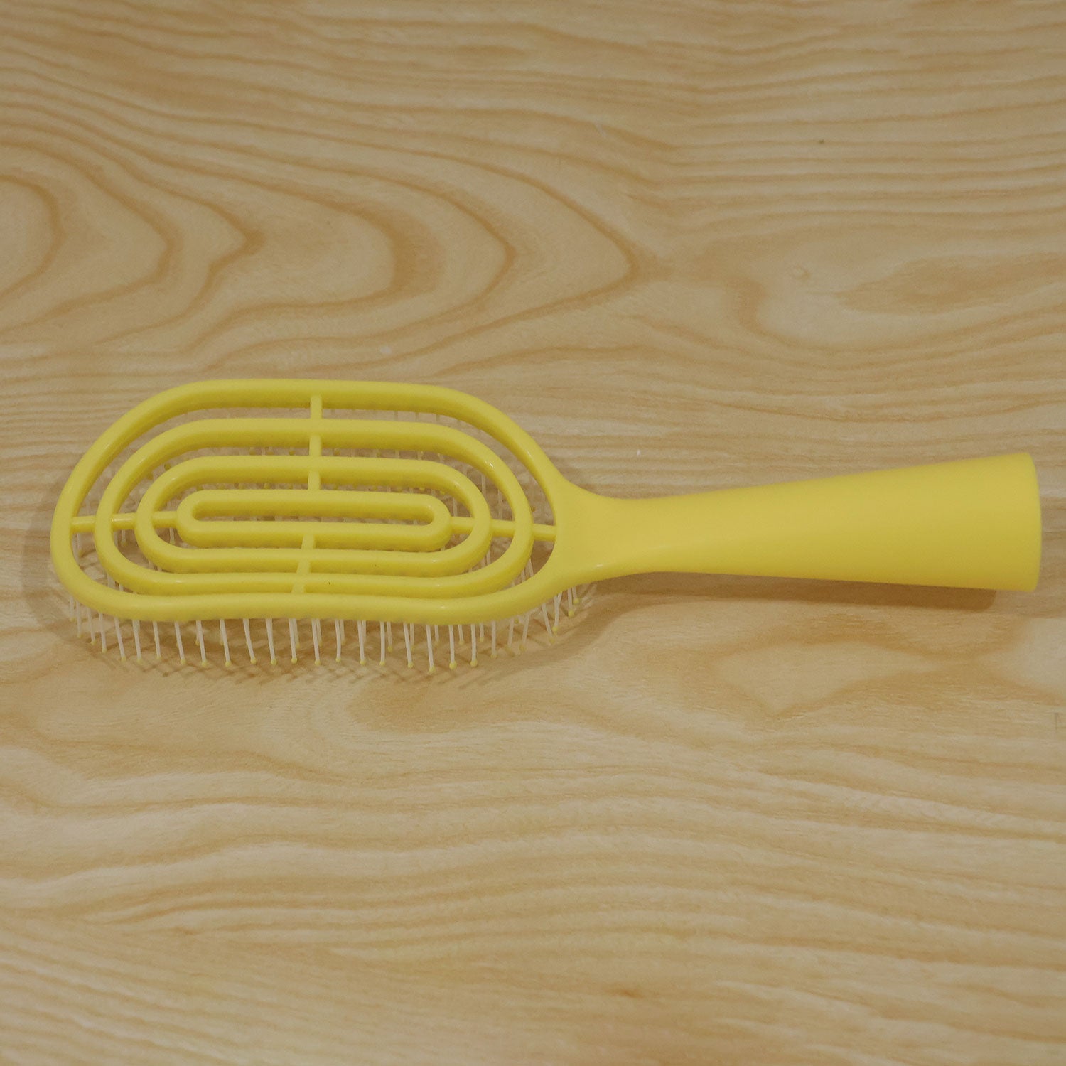 A bright yellow vented detangling brush with white bristles lies flat on a light wood surface.