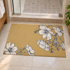 A rectangular mustard yellow bath mat with white line-drawn flowers rests on light-colored bathroom tiles.