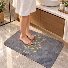 Bare feet are positioned on a grey bath mat with a golden bear graphic in a modern bathroom setting.