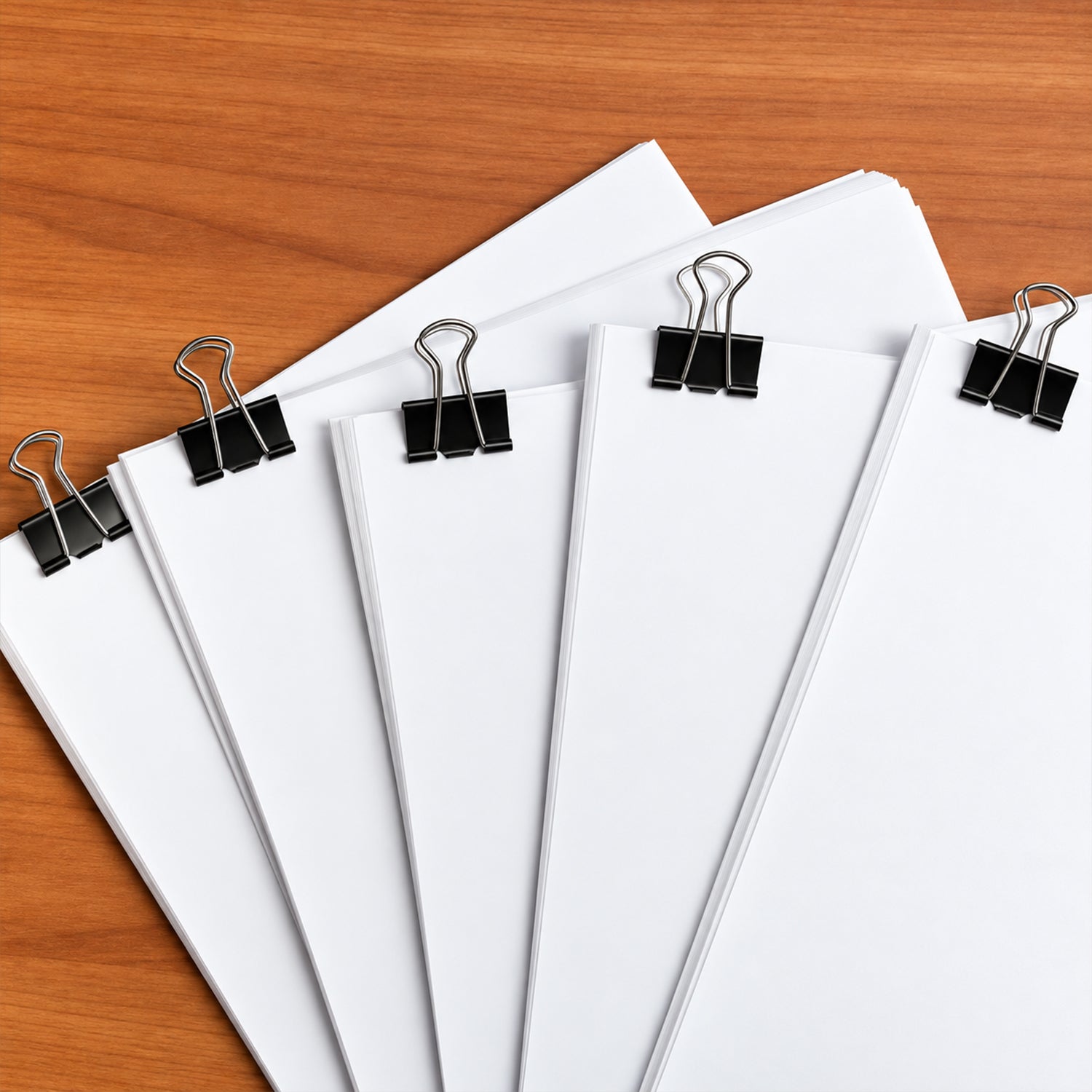 Five stacks of white paper are held together by black binder clips with silver handles on a wooden table.