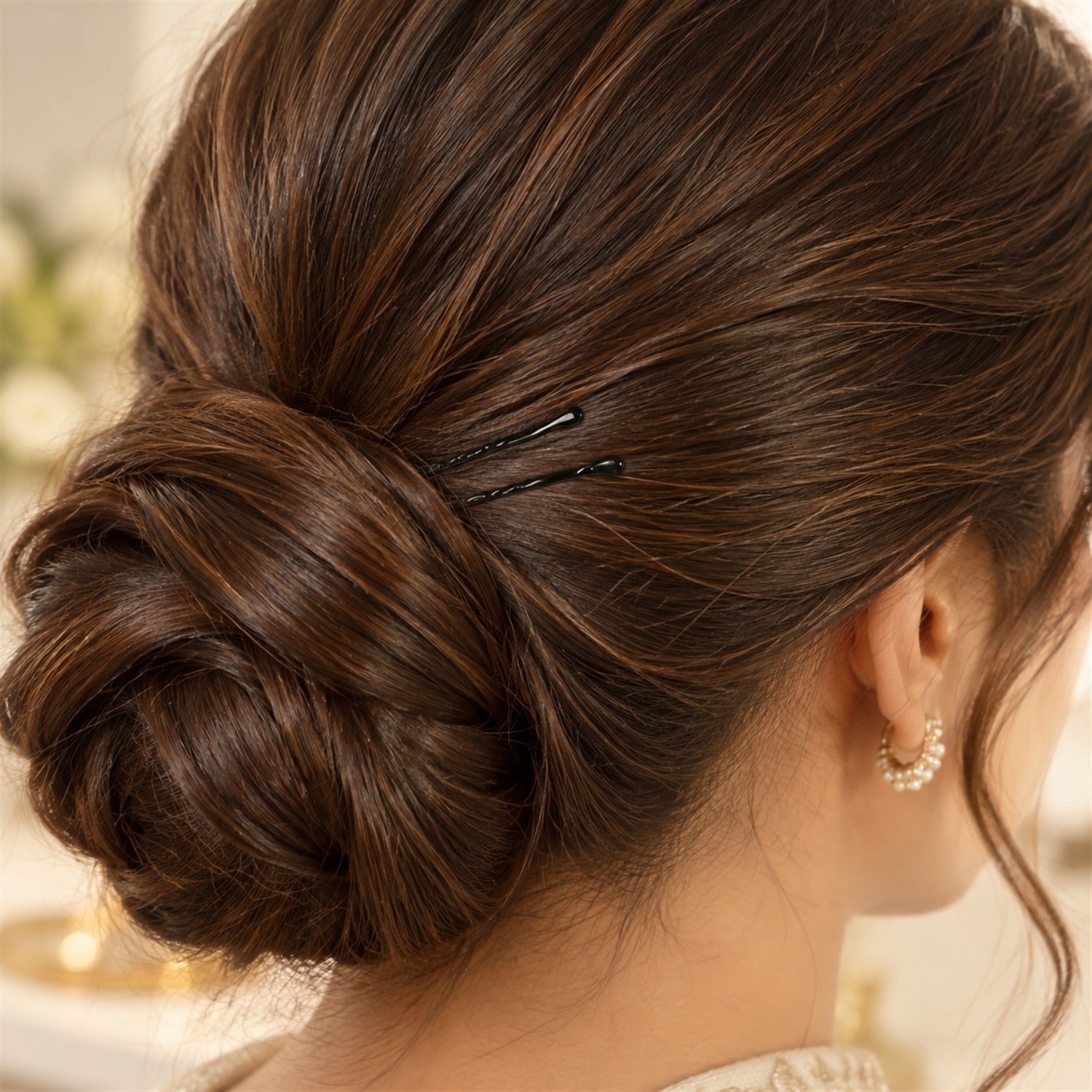 A woman's dark brown hair is styled in a neat bun, secured with two black bobby pins.