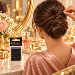 A woman with a neat bun hairstyle inserts a black bobby pin, with a pack of pins on a vanity table.
