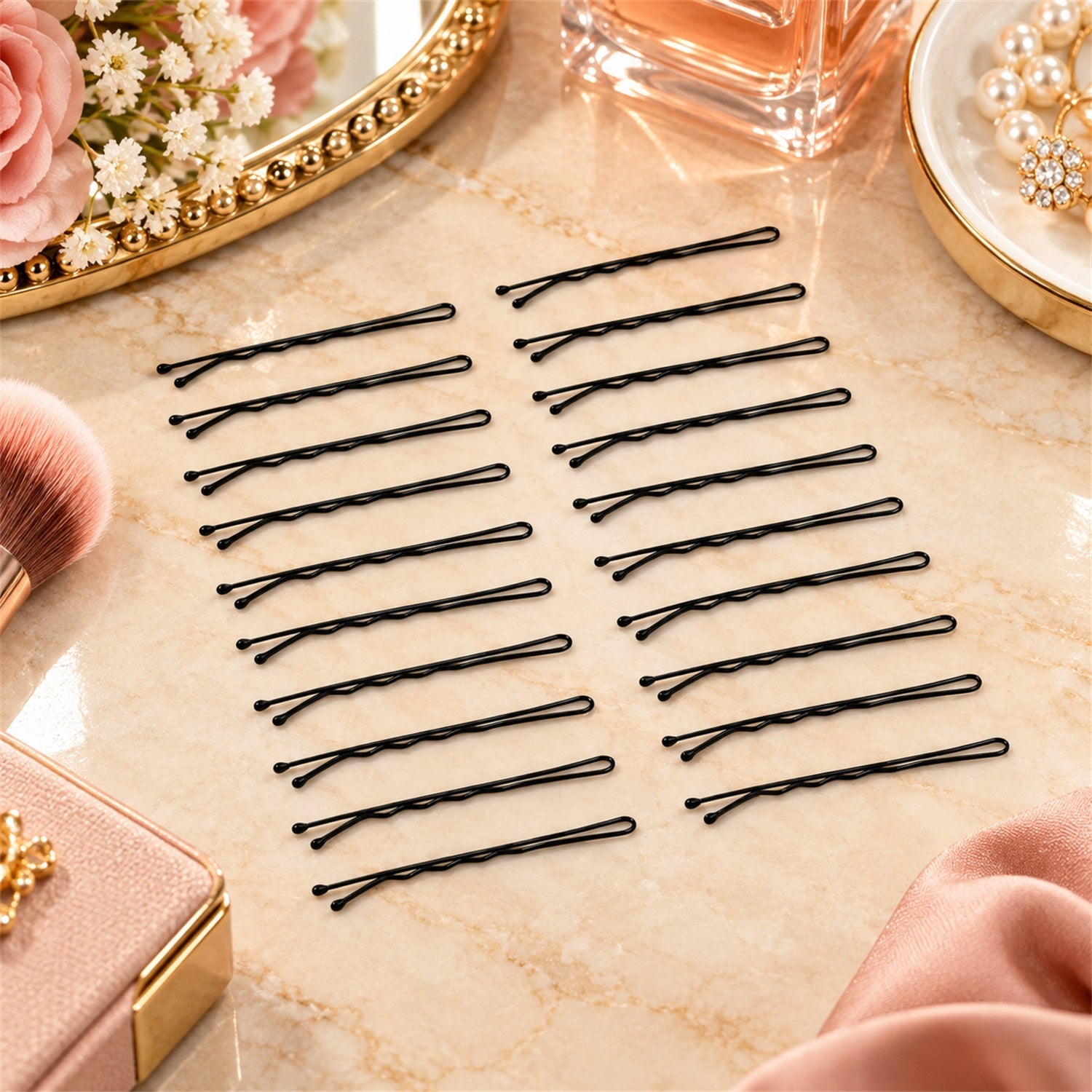 Twenty black metal bobby pins are spread out on a marble surface, surrounded by vanity objects.