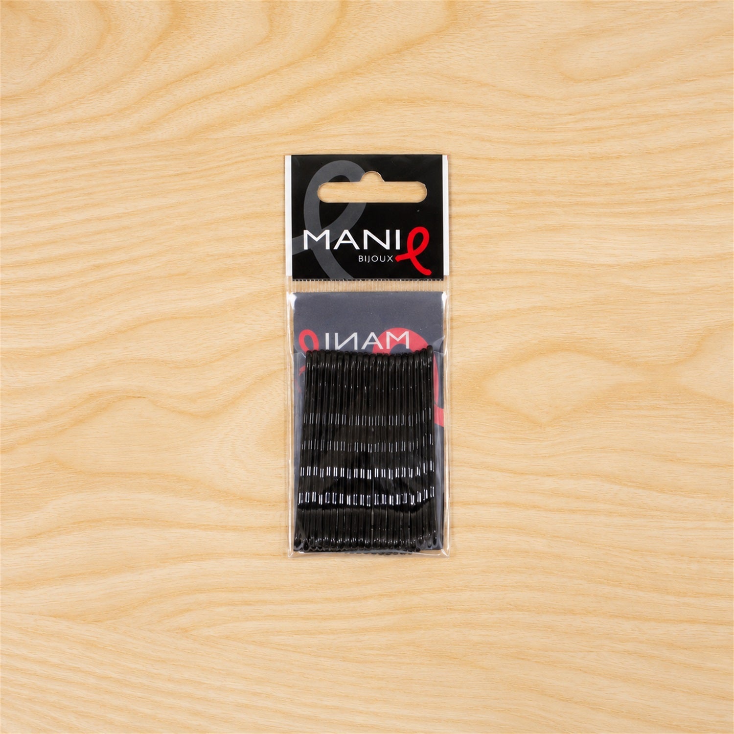 A single clear plastic package containing black bobby pins is centered on a light wooden background.