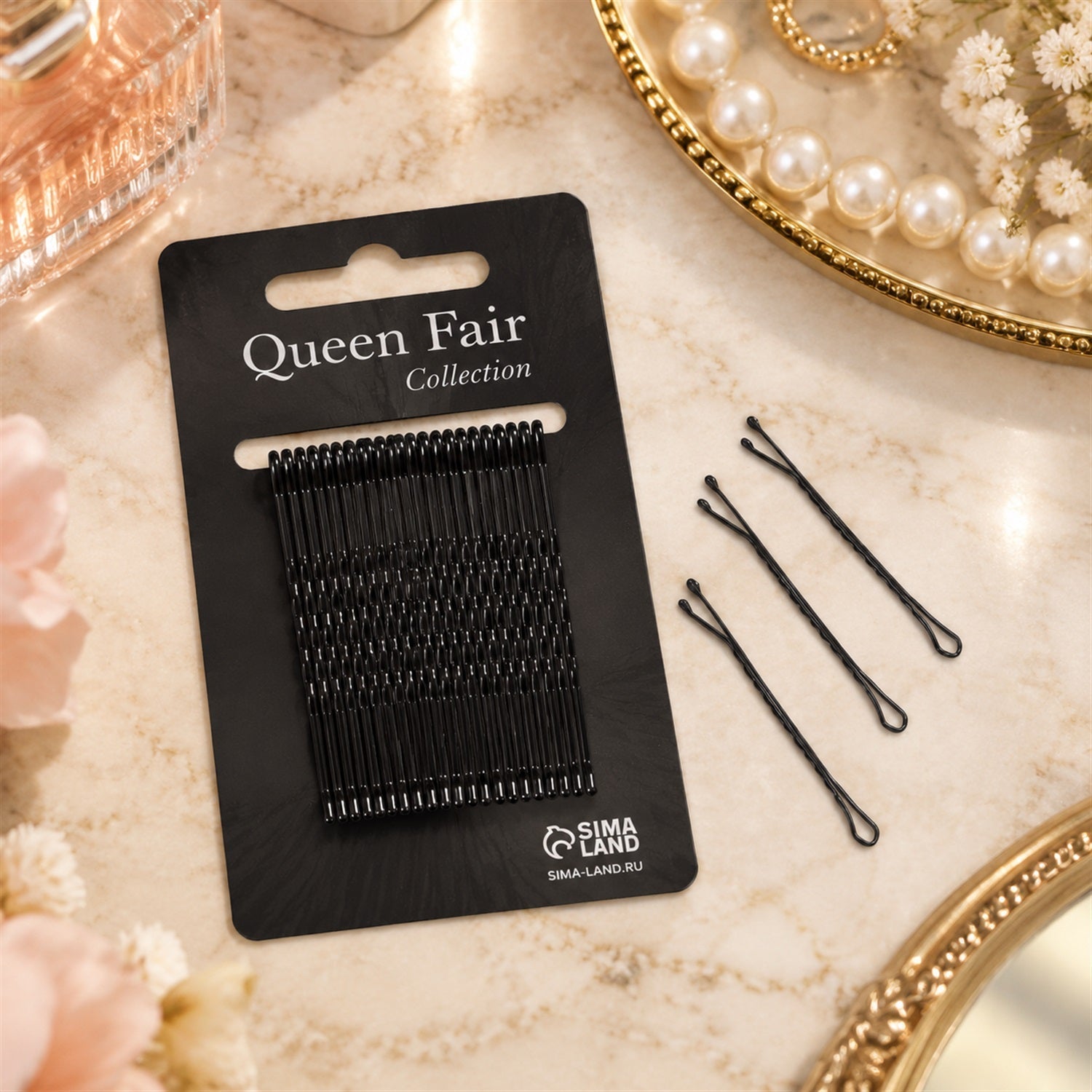 A black card of bobby pins lies on a marble surface with three loose pins beside it and a pearl tray.