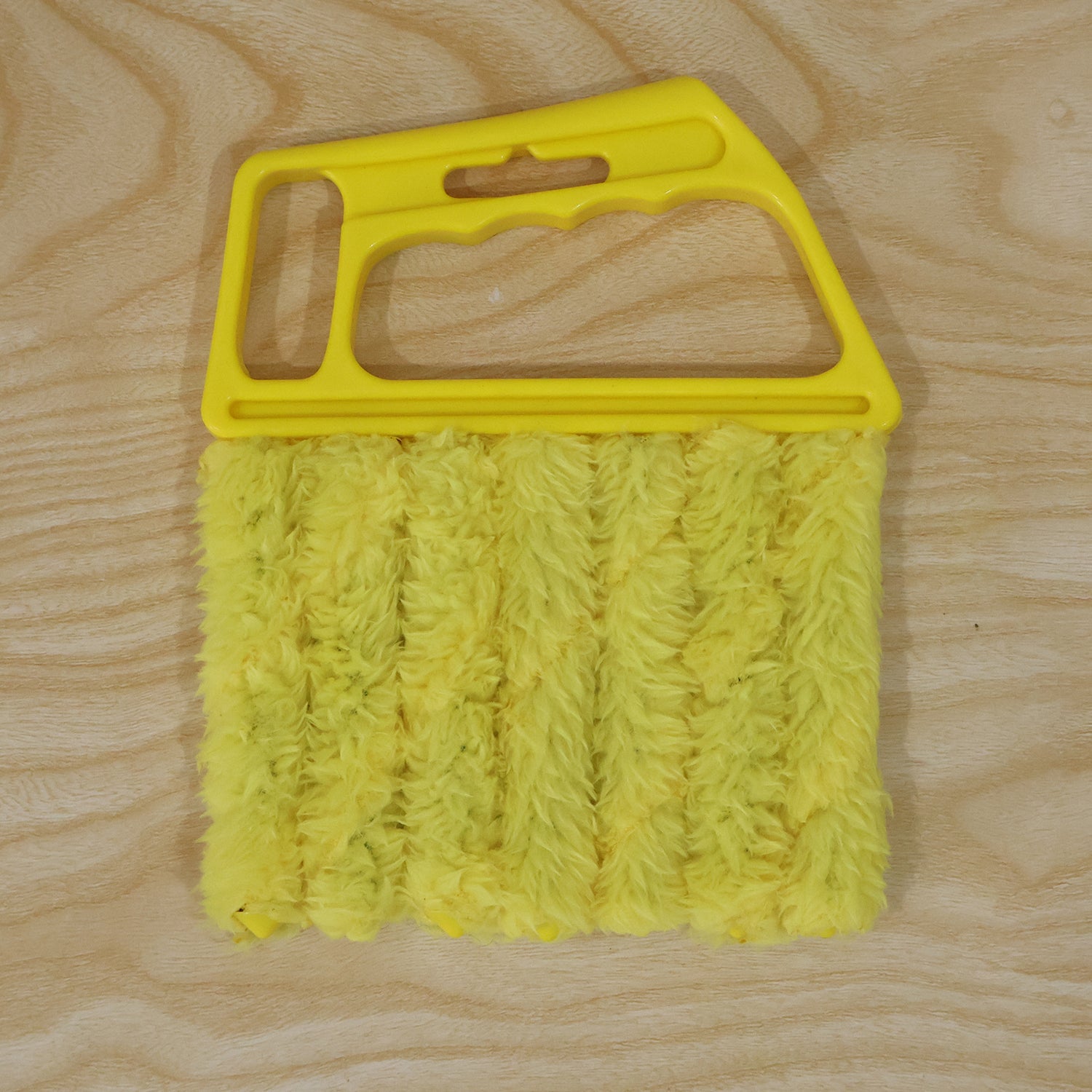 A yellow microfiber blind cleaner with a plastic handle and five microfiber cleaning fingers, on a light wooden surface.