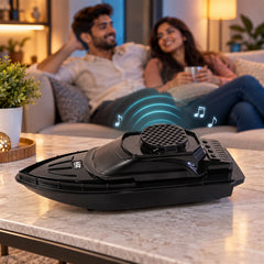 A black boat-shaped speaker on a table, with a smiling couple relaxing on a sofa in the blurred background.