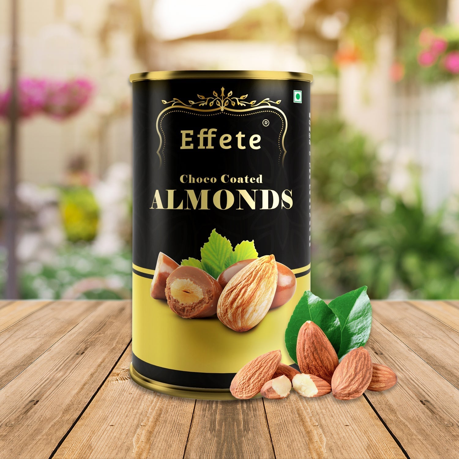 Effete Choco Coated Almonds tin on a wooden table with loose almonds and green leaves in a garden setting.
