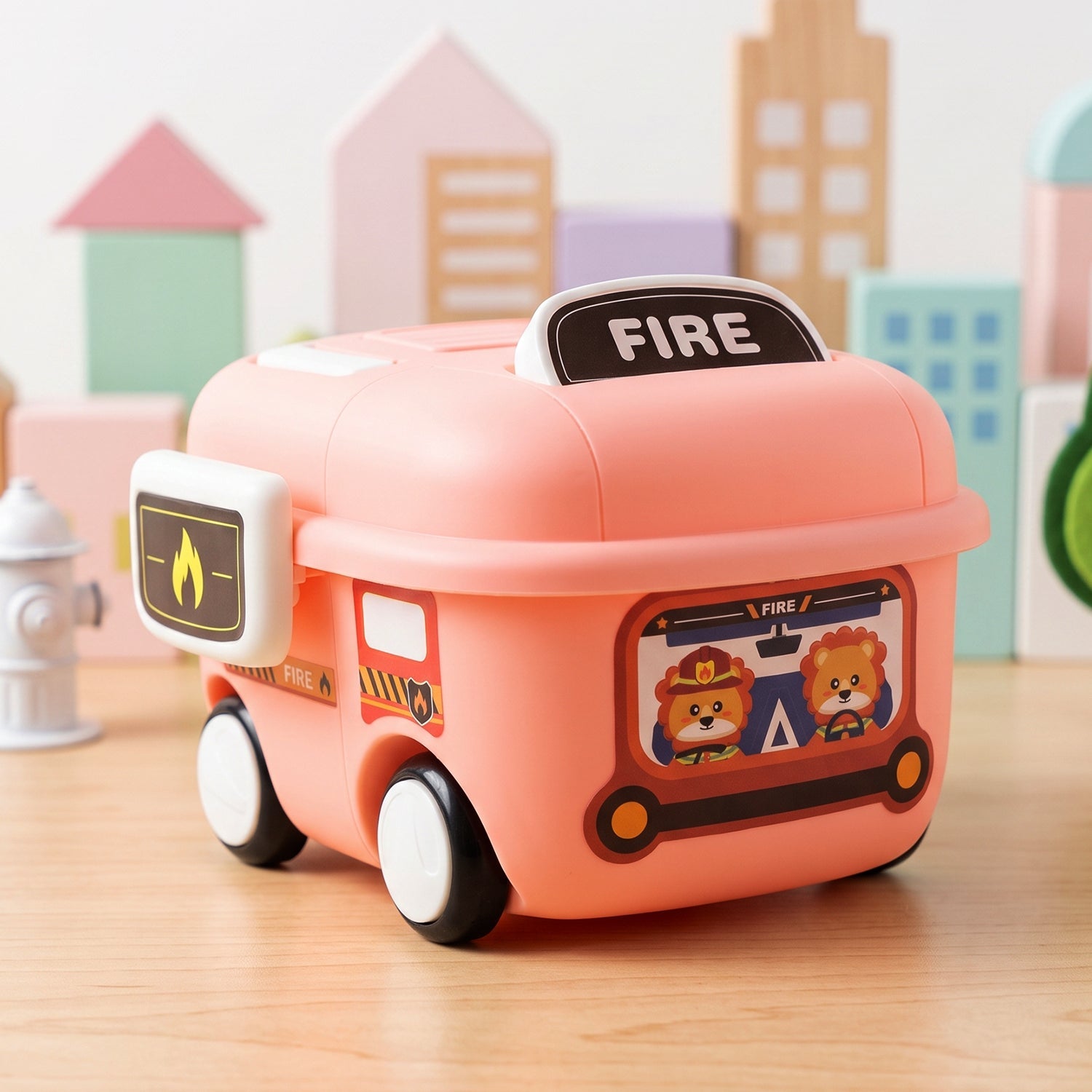 A pink fire truck toy storage box with cartoon animal firefighters on the side sits on a wooden surface with building blocks.