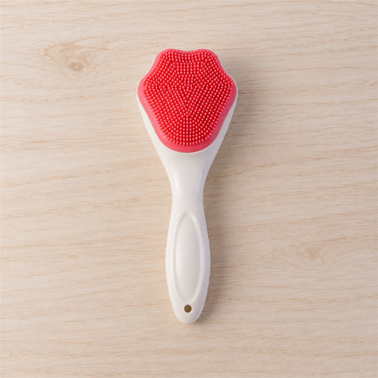 A white-handled brush with a pink, paw-shaped silicone head is positioned centrally on a light wooden surface.