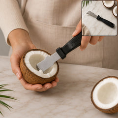 A person uses the Apex tool to remove meat from a halved coconut, with another coconut half nearby.