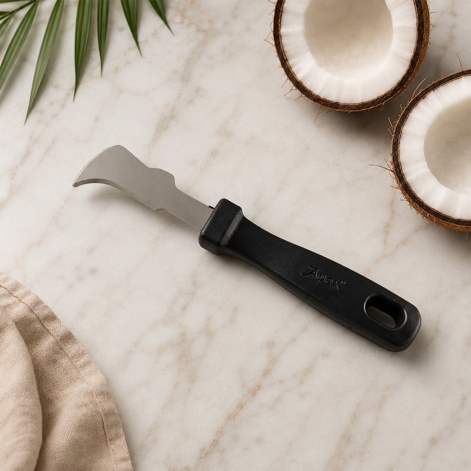 The Apex coconut meat removal tool with a black handle and silver blade lies on a marble surface with coconut halves.