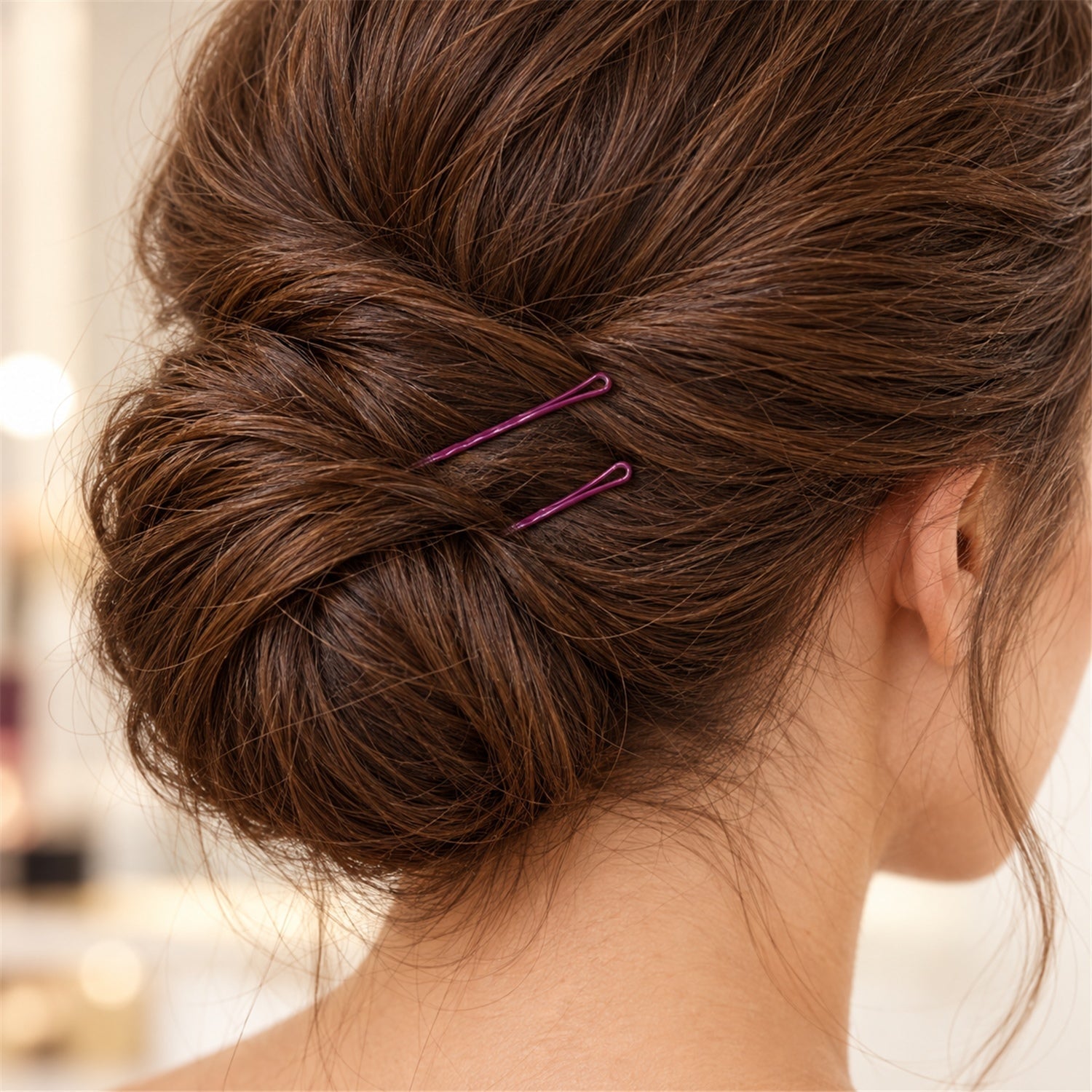 A close-up of a woman's neatly styled brown hair bun, secured with two dark purple bobby pins.
