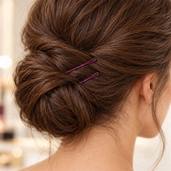 A close-up of a woman's neatly styled brown hair bun, secured with two dark purple bobby pins.