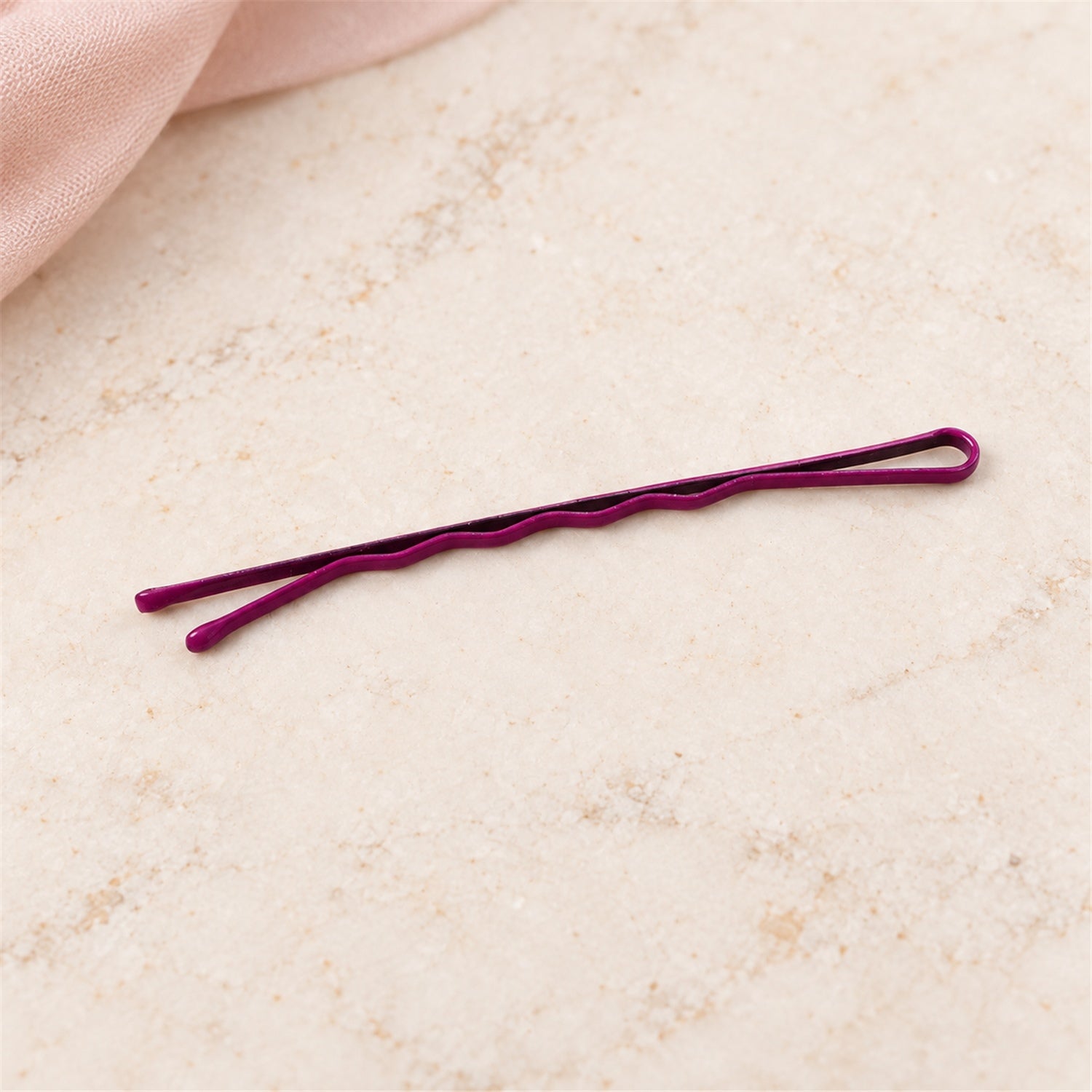 A single dark purple bobby pin with a wavy design rests on a light-colored, textured surface.
