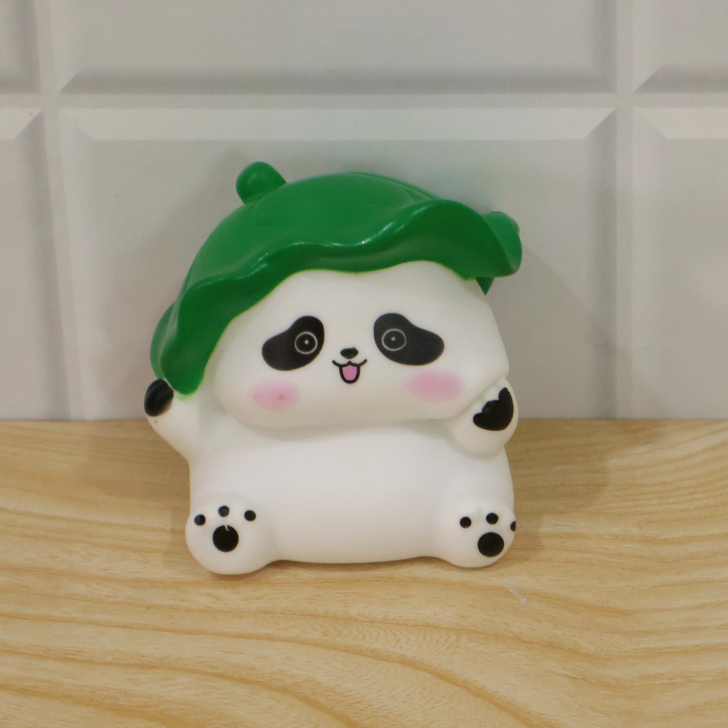 The white panda night light with a green leaf hat is placed on a light wooden surface against a tiled wall.
