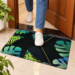 A person in jeans and white sneakers steps onto a black mat with green and blue tropical leaf patterns.