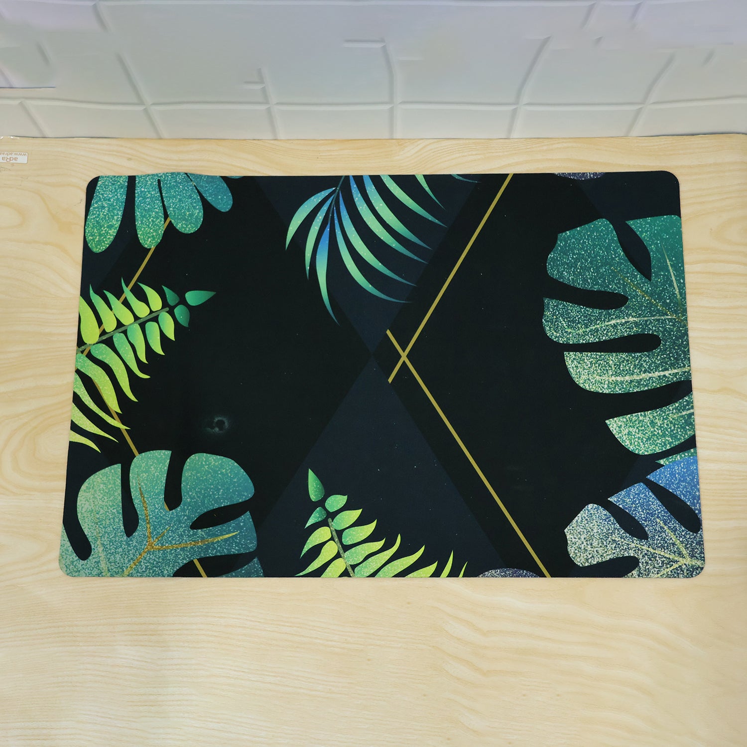 A black mat with green and blue tropical leaf patterns lies flat on a light wooden surface.