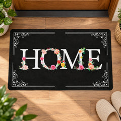 A black rectangular mat with a white and floral HOME design sits on a wooden floor, with slippers nearby.