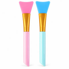 Two silicone face mask brushes, one pink and one blue, stand upright against a white background.