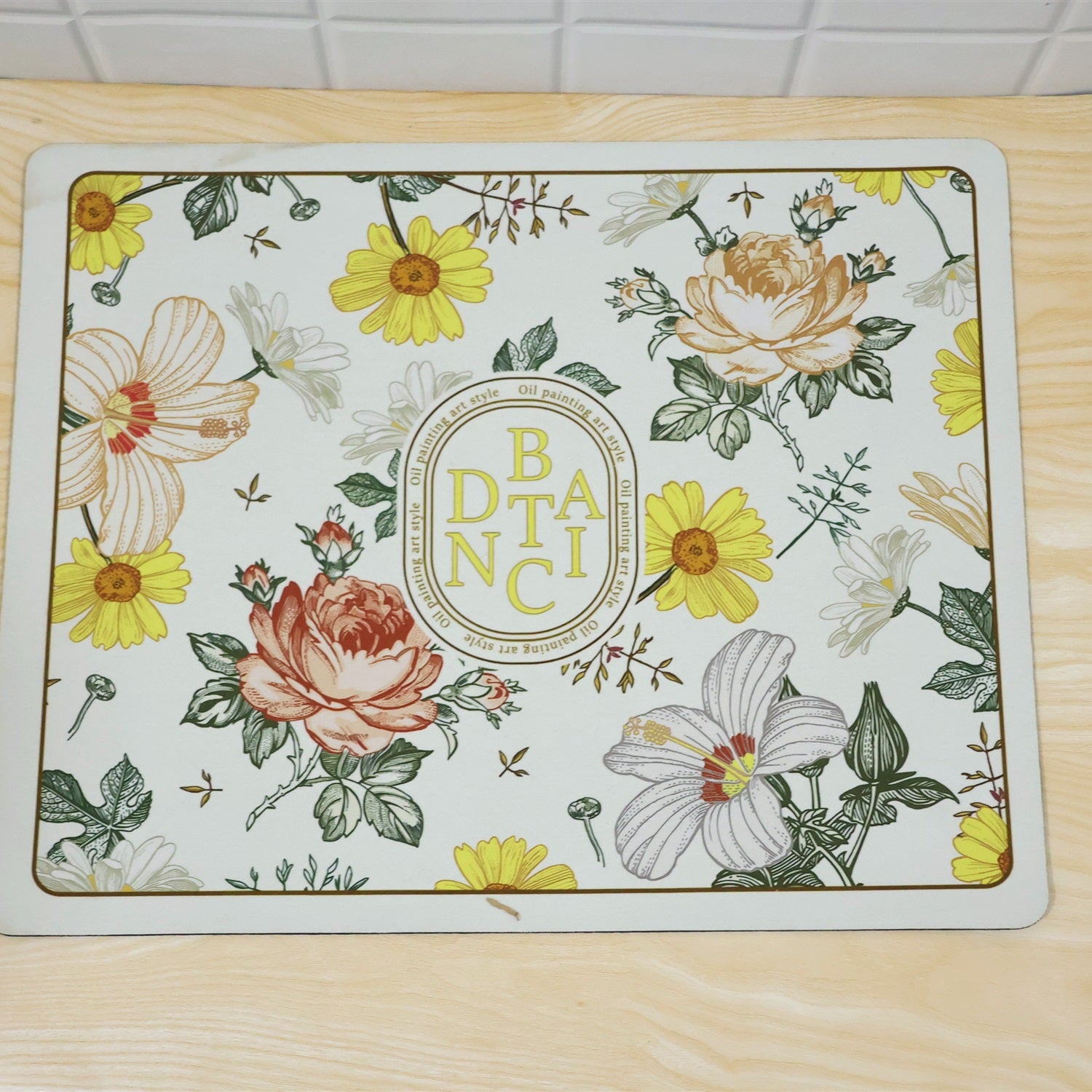 A rectangular bath mat with a detailed botanical print featuring yellow, pink, and white flowers on a light background,