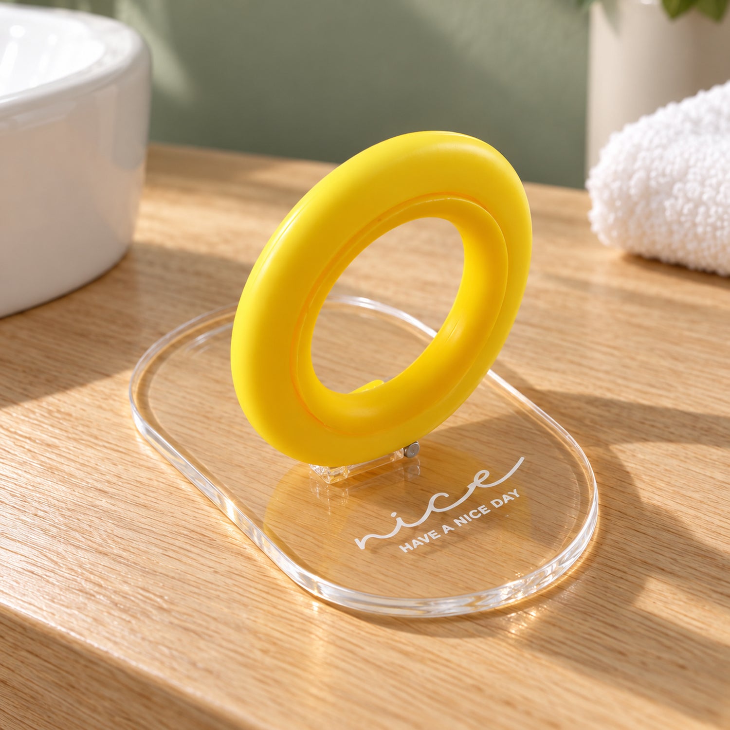 The yellow ring and clear adhesive base toilet seat lifter rests on a wooden countertop next to a white sink.